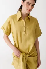 Vestido corto color pistacho, estilo camisa, con cuello clásico, mangas cortas con dobladillo y cierre frontal parcial con botones. Presenta un lazo anudado en la cintura.