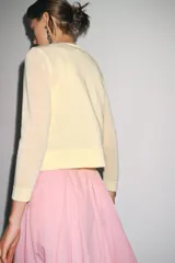 Chaqueta de punto fino color amarillo pastel, con cuello redondo, manga larga y cierre frontal con botones.