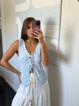 Top tejido de punto color celeste claro, sin mangas, con escote pronunciado en V y cierre frontal mediante lazos anudados. Presenta un patrón texturizado de cuadros.