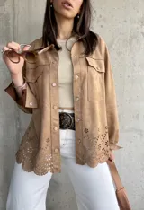 Sobrecamisa color tostado de gamuza sintética, con corte oversize, mangas largas, bolsillos frontales y detalle calado con motivos florales en el ruedo.