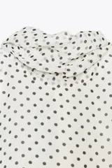Top blanco con estampado de lunares negros, cuello halter con pañuelo y cierre con botón en la espalda.