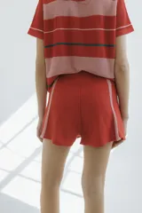 Short tejido en jersey color crudo con cintura elastizada azul marino y cordón rojo. Presenta rayas verticales rojas y laterales en azul marino.