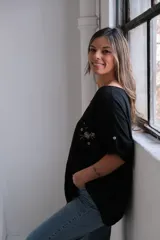 Blusa negra de lino con cuello redondo y mangas 3/4 con detalle de botón. Presenta un bolsillo en el pecho con bordado de lentejuelas y cuentas.