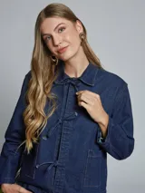 Chaqueta de jean azul con cuello camisero, cierre frontal con lazos y bolsillos de parche.