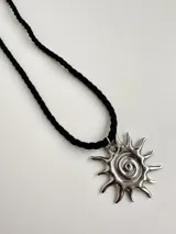 Collar con dije plateado en forma de sol con espiral central, y tiento sailor negro.