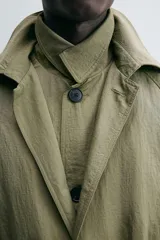 Trench color verde oliva de tejido técnico, corte relaxed fit, cuello solapa, manga larga, bolsillos laterales y abertura en la espalda.