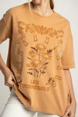 Remera color ocre de corte oversize, con estampado de flores y texto en francés.