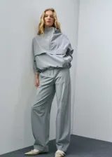 Pantalón gris de tiro medio y corte ancho, con bolsillos laterales, cierre oculto con botón, gancho y cremallera, y forro interior.