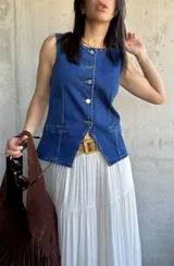 Chaleco de denim azul con escote en V y cierre frontal con botones. Tiene dos bolsillos frontales a la altura de la cintura.