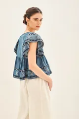 Camisa celeste de corte amplio confeccionada en tencel, con mangas cortas y ruedo con terminación de volado.