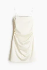 Vestido corto de breteles finos color blanco, con escote recto y frunces laterales que generan un efecto drapeado.