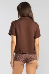 Camisa marrón de lino y Tencel, de manga corta, con cuello camisero y cierre abotonado al frente.