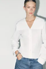 Camisa blanca de algodón con cuello bobo, manga larga con puños y cierre frontal con botones.