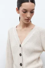Cardigan de tejido de punto color beige melange, con escote en V, manga larga abullonada y cierre frontal con botones oscuros.