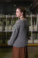 Sweater tejido de lana color gris con cuello redondo y puños acanalados. Presenta un diseño bordado a mano con motivos campestres: sol, vaca, árbol y granero.