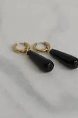 Par de aros colgantes con argolla dorada de acero quirúrgico hipoalergénico y dije en forma de gota de piedra natural blanca.