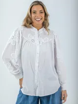 Camisa color crema de broderie, corte holgado, con cuello mao y mangas largas abullonadas con bordados florales.