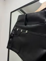 Mini short negro de cuero sintético con tachas plateadas en forma de oso en los bolsillos delanteros y ojales metálicos en los laterales.