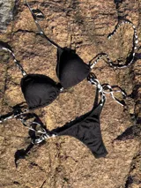 Conjunto de bikini con estampado animal print blanco y negro. El corpiño es de triángulos movibles con tiras finas para atar al cuello y a la espalda, con almohadillas desmontables. La bombacha es colaless con tiras finas para atar a los costados.