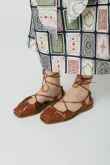 Sandalias chatitas de cuero color bordó, con puntera cuadrada y tiras finas que se atan al tobillo.