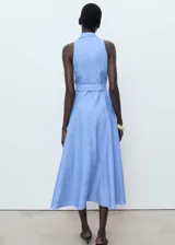 Vestido midi de algodón y lino, color celeste con rayas verticales blancas. Presenta cuello camisero, diseño sin mangas con tirantes anchos, cierre de botones frontales, cinturón con hebilla y falda evasé.