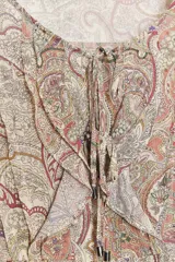 Camisa estampada con motivos paisley en tonos beige, rosa, lila y amarillo. Tiene cuello redondo con lazos, mangas largas abullonadas con puños elásticos y volantes en el delantero.