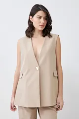 Chaleco largo color beige con solapas, sin mangas y con un botón metálico.
