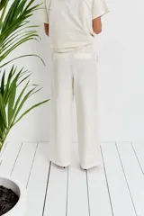 Pantalón de lino color blanco, de corte ancho y tiro alto, con bolsillos laterales y cierre frontal con botón.