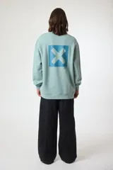 Buzo de cuello redondo color crema, con un pequeño parche cuadrado azul marino con una 'X' blanca en el pecho.