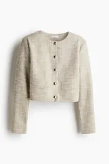Saco corto de tweed color beige, con cuello redondo, cierre frontal con botones dorados y bolsillos delanteros decorativos.