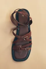 Sandalias planas de cuero color marrón con tiras finas y hebillas doradas.
