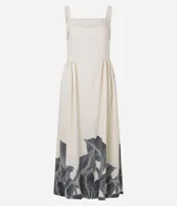 Vestido midi de corte evasé, color crema, con escote cuadrado y breteles anchos. Presenta un estampado grande de hojas y follaje en tonos oscuros en el ruedo inferior.