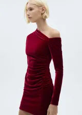 Vestido corto de terciopelo color borgoña, con un hombro descubierto y manga larga en el otro brazo. Presenta un drapeado lateral que estiliza la figura.