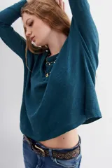 Remera de manga larga, color verde azulado oscuro, confeccionada en algodón peruano jaspeado. Presenta una moldería holgada con mangas que se ensanchan bajo el brazo y terminan ajustadas en la muñeca.