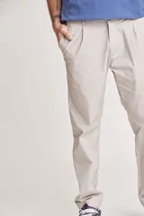 Pantalón de vestir color beige, de corte recto, con bolsillos laterales y traseros. Se ajusta a la cintura con cinturón de cuero marrón.