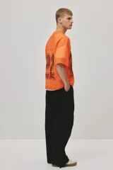 Remera de malla color naranja vibrante, estilo jersey de fútbol americano, con cuello en V y corte oversized. Presenta un estampado grande y desgastado del número "22" en color negro o marrón oscuro en el frente.