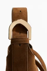 Cartera marrón de gamuza sintética con correa fina ajustable y asa ancha con hebilla metálica dorada.