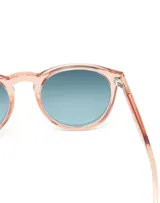 Gafas de sol Hawkers modelo Bel Air, unisex, con montura redonda color rosa claro transparente y lentes degradadas de azul a transparente.