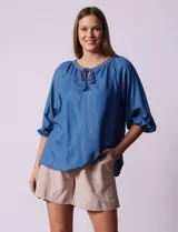 Blusa celeste de tencel con cuello a la base, escote en V con aplique de cordel y lazo de ajuste. Manga larga amplia con puño elastizado.
