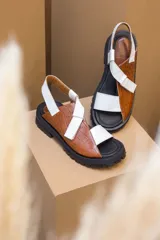 Sandalias de cuero color marrón y blanco, con suela track negra y ajuste con velcro.