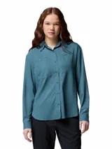 Camisa de senderismo de manga larga color azul verdoso, con protección solar FPS 50, tejido absorbente de sudor y ventilaciones de malla. Cuenta con dos bolsillos frontales con cierre, tapeta abotonada y lazo para colgar.