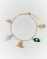 Dije charm colgante de oro con forma de trébol de cuatro hojas, llave y piedra verde. El dije se engancha a una cadena de oro con pequeñas cuentas.