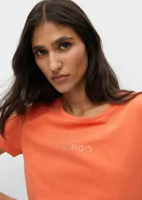 Camiseta de algodón color naranja con logo Mango estampado en el pecho. Diseño recto, cuello redondo y manga corta.