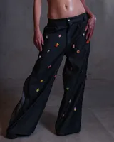 Pantalón de denim negro con cierres laterales a lo largo y decorado con pines coloridos.