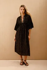 Vestido largo negro con estampado de lunares dorados, mangas al codo y corte amplio con ajuste elástico en la cintura. Presenta bordados de lentejuelas y mostacillas en el escote y mangas.