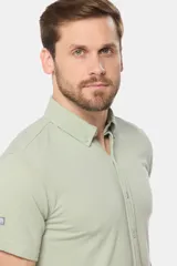 Camisa de piqué color verde claro, de manga corta, con botones personalizados y logo bordado a tono.