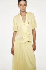 Camisa color amarillo claro de popelín con lyocell, cuello redondo con escote pico, manga corta con elástico y cierre frontal con lazadas.