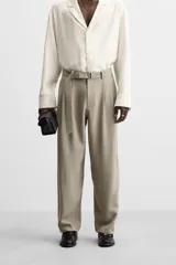 Pantalón negro de corte amplio, con pliegues frontales, bolsillos laterales y traseros de ojal. Incluye cinturón de la misma tela con hebilla metálica.