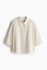 Camisa color crema en tejido liviano de lino y viscosa con cuello, botones adelante y pliegue de caja invertido en la espalda. Modelo de corte holgado con hombros marcadamente caídos, mangas al codo y bajo levemente redondeado.