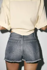 Shorts de jean de algodón, tiro alto, color azul claro desgastado. Presenta cinco bolsillos, cierre frontal con botón metálico y bajo desflecado con vuelta.